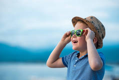海滩上戴太阳镜的快乐孩子的画像。暑假的概念。在海边边戴帽子和眼镜笑着的小男孩