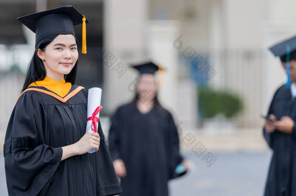 一名身穿毕业礼服的年轻貌美的亚洲女大学毕业生在参加完大学毕业典礼后，持<strong>学位证</strong>书站在大学大楼前