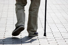 一个拿着手杖走在街上的人。老年、脊柱疾病或关节疾病、老年人的概念