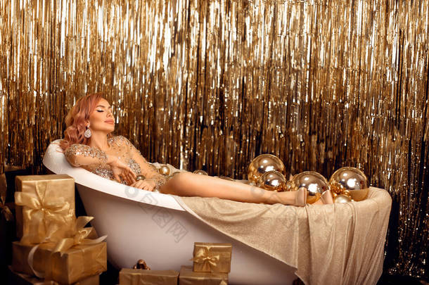 在金制的圣诞礼物和浴缸里的球上挂着奢华女人的肖像。美容美发<strong>模特</strong>，妆容华丽，头发飘逸，头戴<strong>珠宝</strong>，穿着金银<strong>珠宝</strong>，衬托着亮丽的黑色背景.