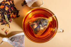 红茶、香草和水果在透明的杯子中酿制而成.用茶袋酿制的茶。天然健康饮品的概念。米色背景茶袋