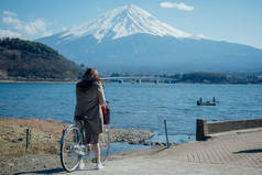 一名妇女在日本山崎市川口湖停放自行车，拍了一张照片，富士山在后面.