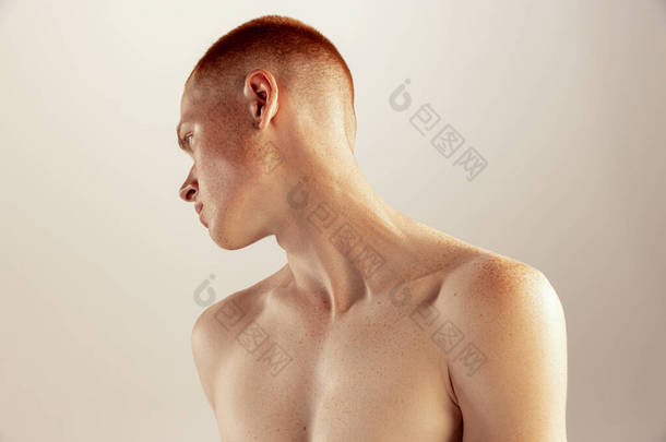 年轻红头发男子的画像，在灰色的工作室背景下，一丝不挂地显得孤立无援。有质感的锁骨男性健康、生活方式、美感、身体和皮肤护理的概念。有雀斑的模型