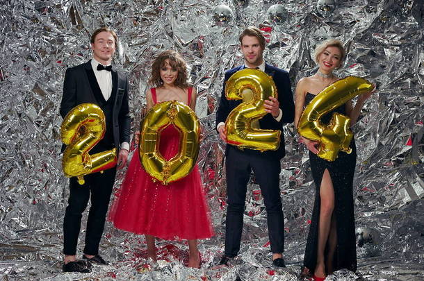 Four Young People At Party. Two Men In Suits And Two Girls In Evening Dresses. New Year Celebration.