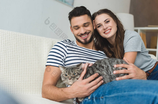 愉快的年轻夫妇与逗人喜爱的<strong>小花猫</strong>坐在长沙发