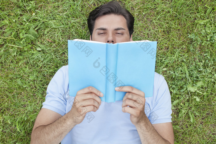 清新草地看书的男人摄影图
