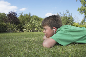 男孩戴着耳机<strong>趴在</strong>草坪上