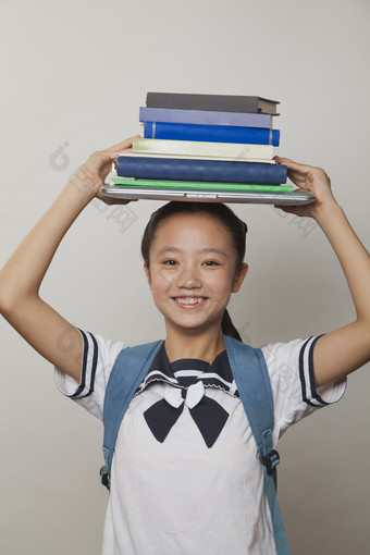 <strong>学生</strong>小女孩校服背着书包头顶着书本学习微笑