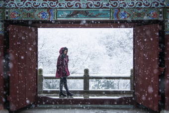 穿着冬装的女孩子在红色大门外看雪景