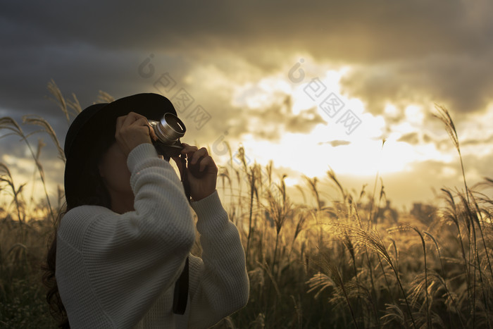 夕阳下拿着相机拍照的女孩