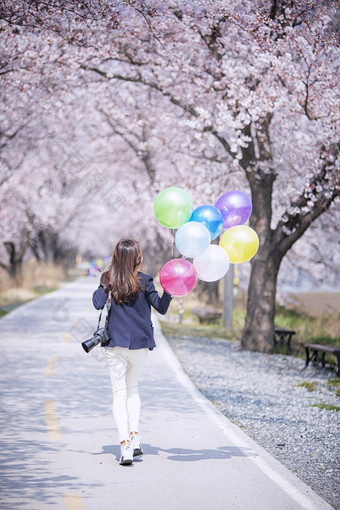 女子拿着气球走在樱花林