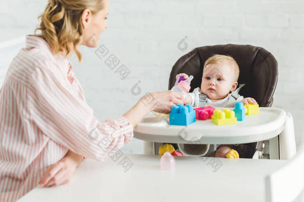 母亲喂养婴儿的女儿坐在婴儿椅与塑料块