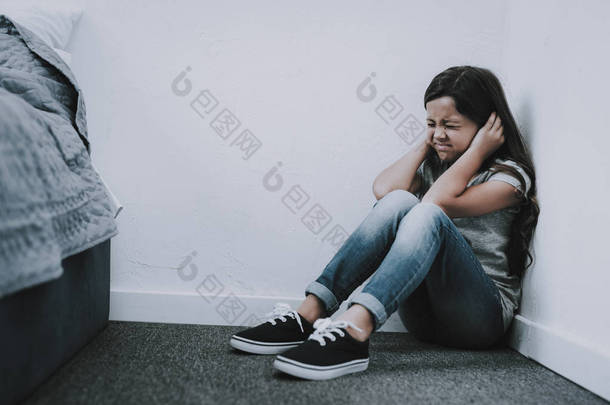 哭泣的女孩坐在地板上关闭耳朵和眼睛。特写镜头的恐惧不愉快皱着眉头黑色头发的白人小孩坐在地板上, 穿着灰色 t恤