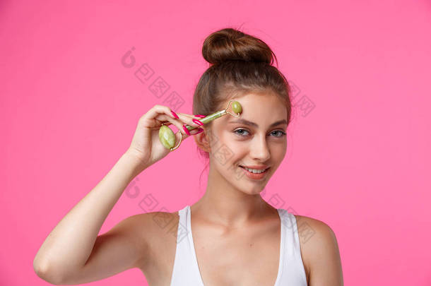 年轻女子应用玉辊按摩她的脸。每日面部护肤治疗，抗年龄程序，以<strong>更好</strong>地保湿，淋巴排水，肤色改善和减少皱纹