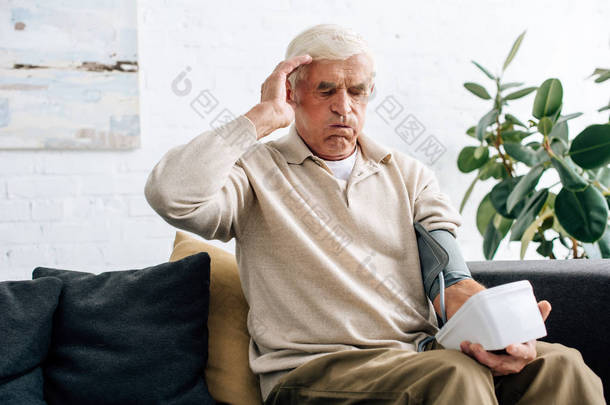 老年人震惊地测量血压，坐在公寓的沙发上 