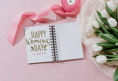 在记事本, 粉红色丝带和白色郁金香在粉红色的快乐母亲节日问候的顶部视图