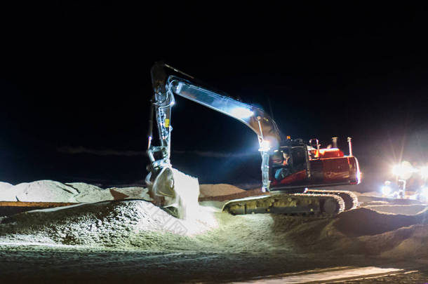 地面工人在黑暗中夜间工作, 挖掘机在海滩上移动沙子进行维护