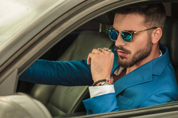 聪明的休闲男子与太阳镜和蓝色西装驾驶他的灰色<strong>汽车</strong>, 肖像图片