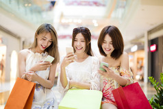 幸福的年轻女人，看着智能手机在商场里