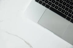 在白色大理石表面上带有黑色键盘的笔记本电脑的顶部视图