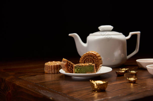 传统美味的<strong>中国</strong>月饼, 茶壶和金锭在木桌上隔离在黑色