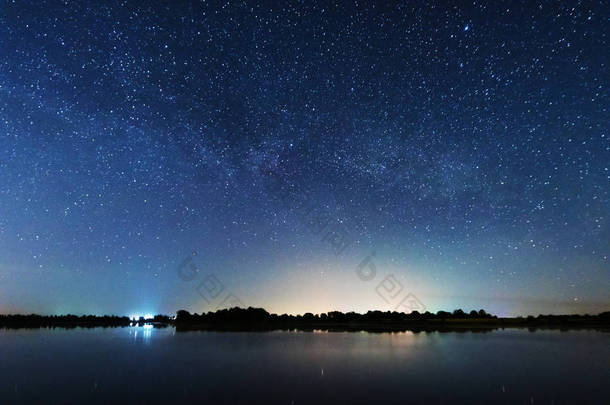 在河岸上的一个迷人的星夜，有一棵大树，天空中的一条银河，夏天有<strong>流星</strong>坠落.