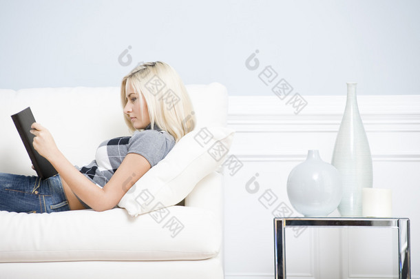年轻女子躺在沙发看书