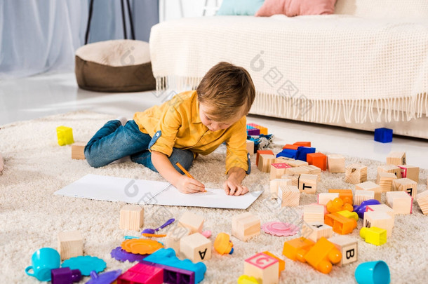 可爱的孩子躺在地毯上, 用铅笔画画