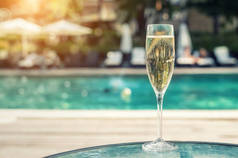 在度假期间，豪华度假酒店在泳池边提供白色香槟或散装玻璃。带上升气泡的起泡酒，室外有蓝色泳池背景。清凉酒精饮品