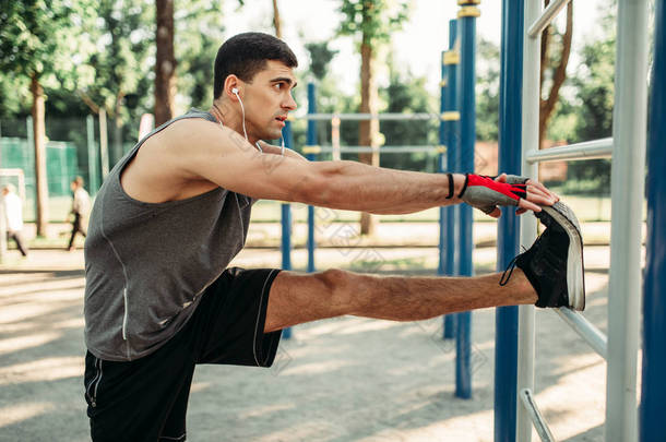 运动男子做伸展腿运动使用水平棒, 户外健身锻炼。健美运动员在夏季公园运动训练中的研究