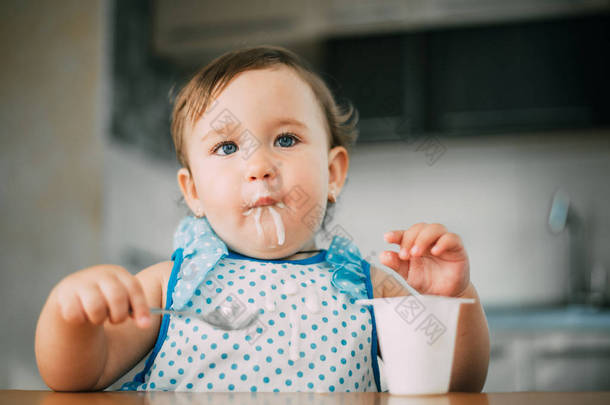 可爱,有趣的女孩吃酸奶在白天在厨房在蓝色礼服