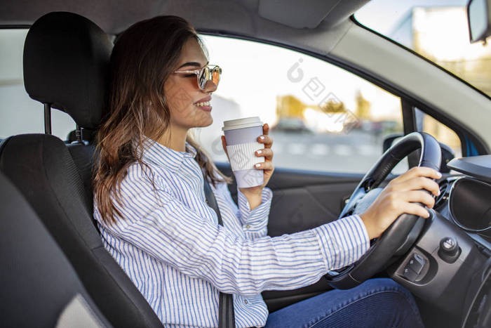 快乐的年轻女人喝咖啡去开车女人开车时喝了