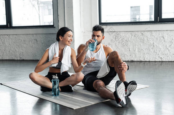 运动的年轻夫妇喝水和休息瑜伽垫后, 在健身房锻炼