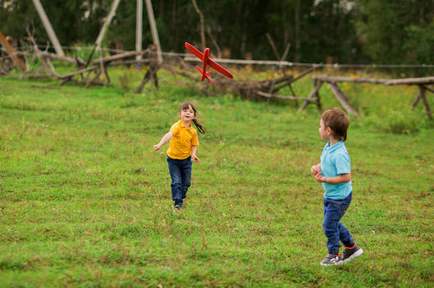 孩子们- -一个穿蓝色T恤的男孩和一个穿黄色衣服的女孩在自然界中扮演一个泡沫塑料玩具红色飞机