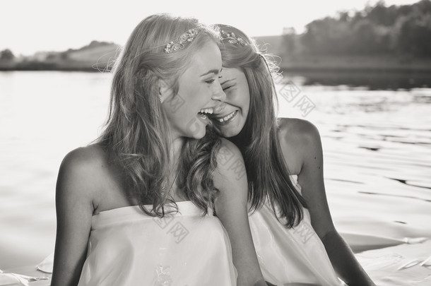 Black and white photography of 2 beautiful princess young ladies in white dresses on summer water ou