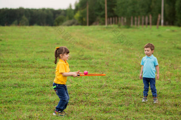 孩子们- -一个穿着蓝色T恤的男孩和一个穿着黄色球衣、带着球拍和球拍的女孩在一起打网球.
