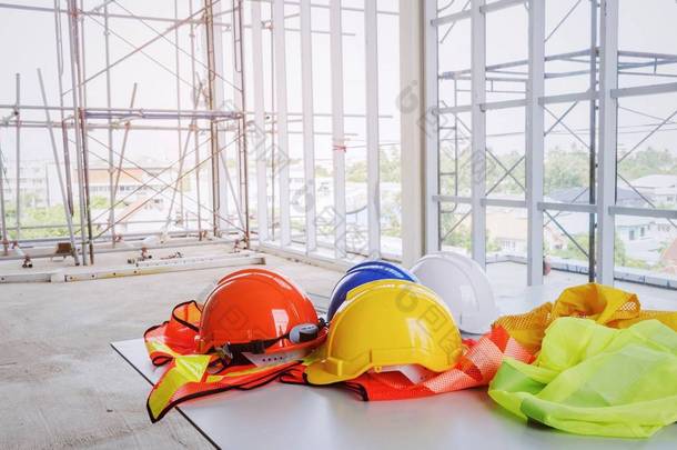 白色, 橙色, 黄色和蓝色安全头盔, 反光衣物在建筑工地和脚手架背景, 工程师, 安全, 工业和建筑建筑概念