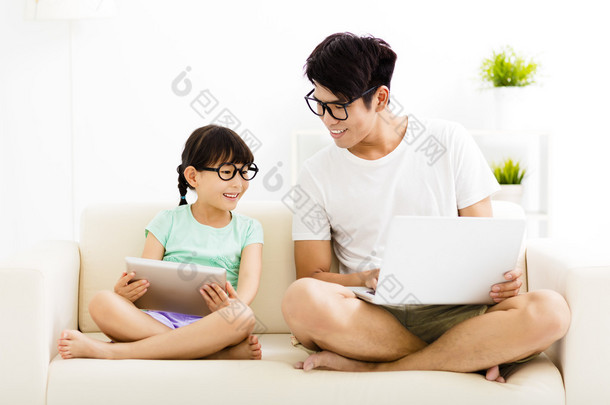 <strong>快乐</strong>的父亲和女儿在沙发上使用笔记本电脑