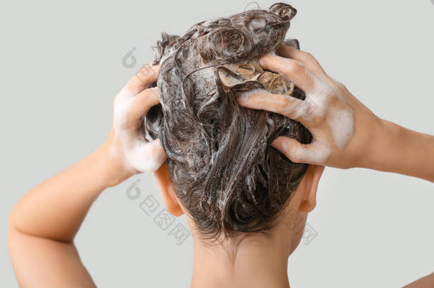 美丽的年轻女子洗头发在灰色的背景，后视图