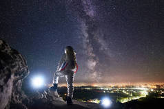 可以看到太空旅行者站在岩石山上，欣赏着星空、银河和夜城的美景。身穿白色宇航服的飞行任务专业宇航员。空间旅行的概念