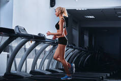 年轻漂亮的竞技女人在健身房的跑步机上