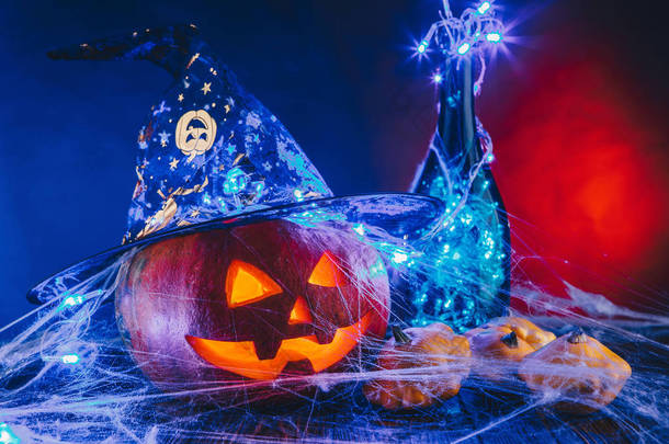 万圣节<strong>南瓜</strong>帽子在蜘蛛网上用糖果和昏暗的灯光。蓝色和红色的背景上捣蛋的概念