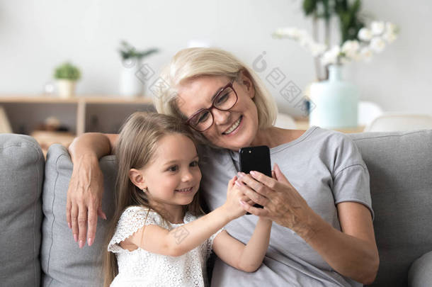 快乐的祖母和可爱的孙女使用手机制作 