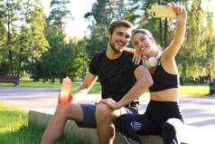 身穿运动服的年轻夫妇坐在城市公园的栏杆上，在夏日阳光灿烂的日子里锻炼完后自拍.