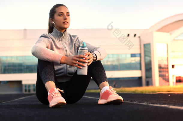 美丽的年轻女子穿着运动服在运动运动后在体育场户外运动喝水
