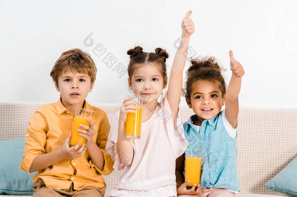 可爱的多民族儿童拿着一杯果汁, 并显示竖起大拇指 