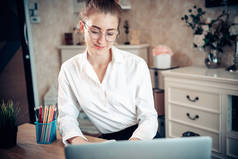 在家里工作时，有魅力的女人在笔记本电脑上工作，这是从家庭生活方式和网上交易中产生的。商务自由人通过她家里的互联网交流，新的正常生活方式