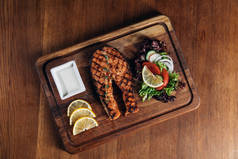 美味的烤鲑鱼牛排在木板上配上柠檬片和沙拉