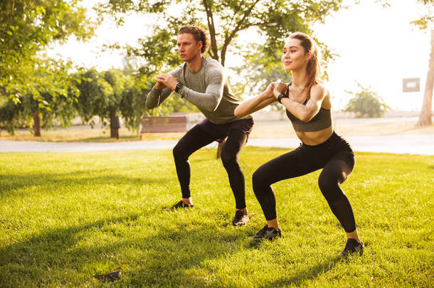 年轻的白种人运动的男人和女人的形象20s 在运动服做锻炼和<strong>蹲</strong>在绿色公园在晴朗的夏天天