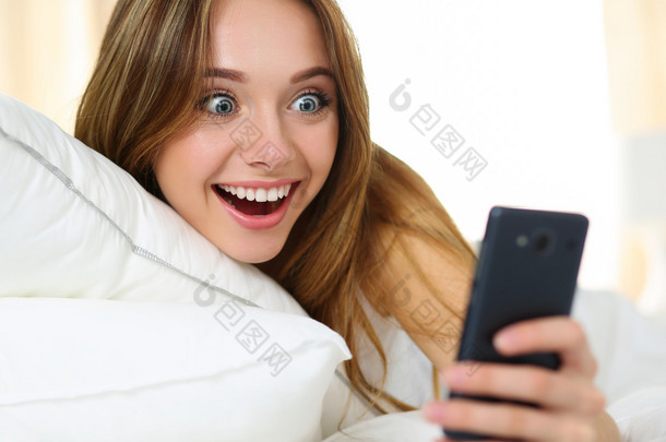 年轻漂亮的金发女人躺在床上，拿着手机